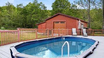 Una piscina al aire libre con una cubierta de madera, una cabaña roja y un área cercada.