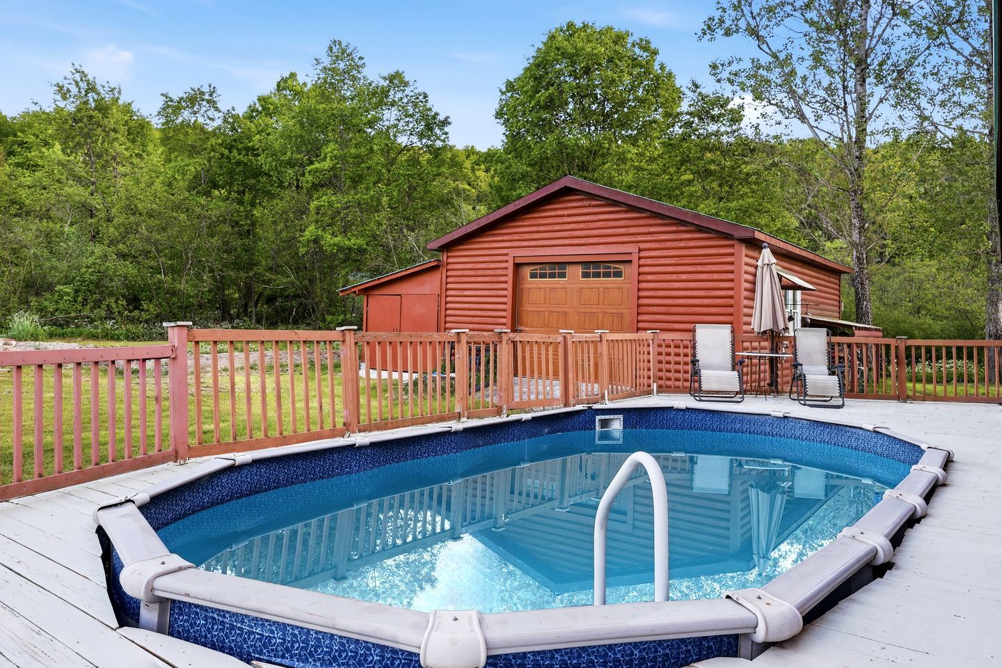 An outdoor swimming pool with a wooden deck, a red cabin, and a fenced area.