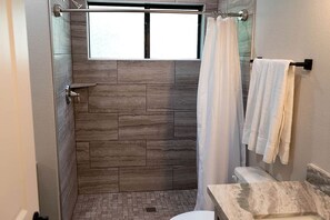 Een badkamer met een douche, een raam en een handdoekhouder.