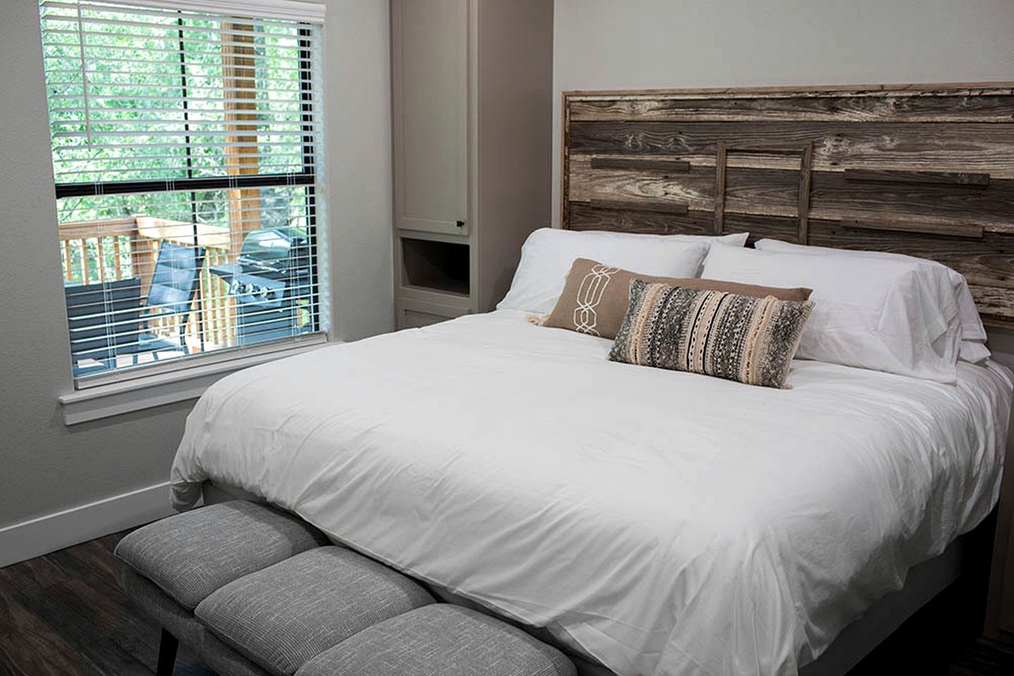 Un dormitorio con una cama grande, un banco, una ventana con persianas y vistas a muebles de exterior.