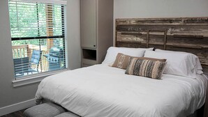 Ein Schlafzimmer mit einem großen Bett, einer Bank, einem Fenster mit Jalousien und Blick auf Gartenmöbel.