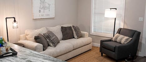Una sala de estar con sofá, sillón, mesa de centro, lámpara y ventana con persianas.