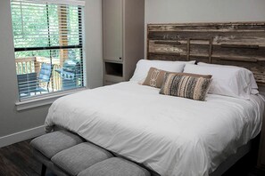 Ein Schlafzimmer mit einem großen Bett, einer Bank, einem Fenster mit Jalousien und Blick auf Gartenmöbel.