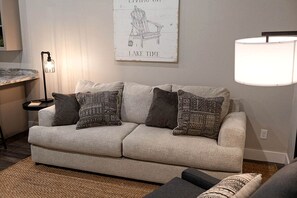 A living room with a sofa, patterned cushions, a lamp, and a wall sign. - Quaint Cabin Ideal for a Secluded Getaway in Livingston, Texas (Livingston)