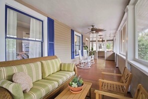 A covered porch with a green striped sofa, wooden chairs, and a ceiling fan. - The Veranda at Wares Creek - Sleeps 12, Pet-friendly, minutes to Gulf beaches! (Bradenton)