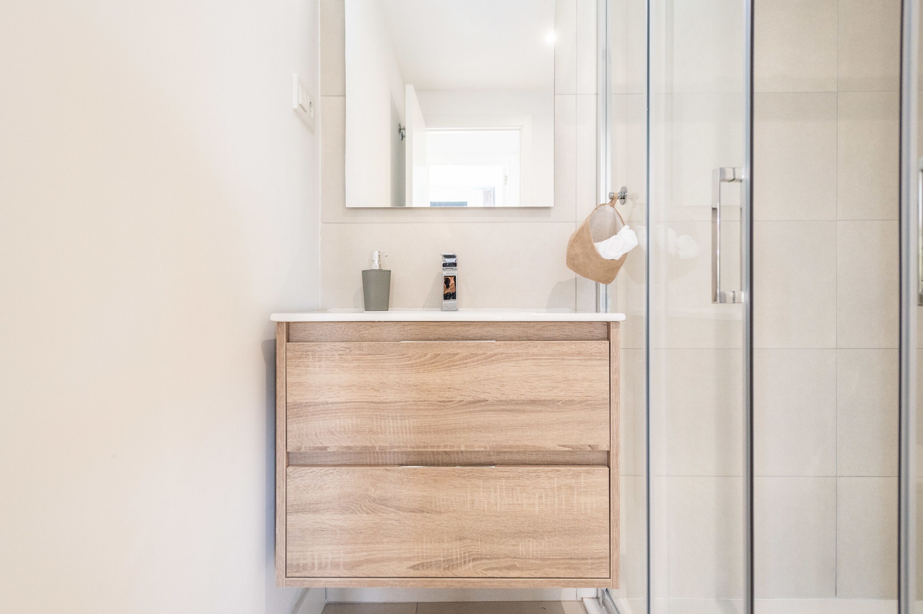 A modern bathroom with a wooden vanity, a glass shower enclosure, and a large mirror.