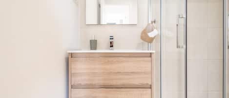 A modern bathroom with a wooden vanity, a glass shower enclosure, and a large mirror.
