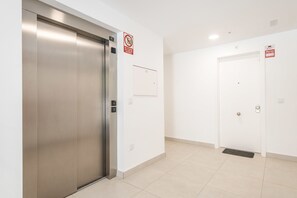 Ein moderner, sauberer Aufzug mit Metalloptik, einem Rauchverbotsschild, einem Feueralarmschild und einer Tür mit Fußmatte.