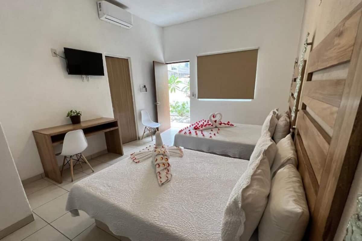 A hotel room with two beds, a desk, a chair, a TV, and a window.
