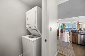 A laundry area with a front-loading washer and dryer, a kitchen with a stainless steel dishwasher, and a view of the ocean through large windows. - Spectacular view of the Gulf and just steps away from the pool and beach! (Miramar Beach)