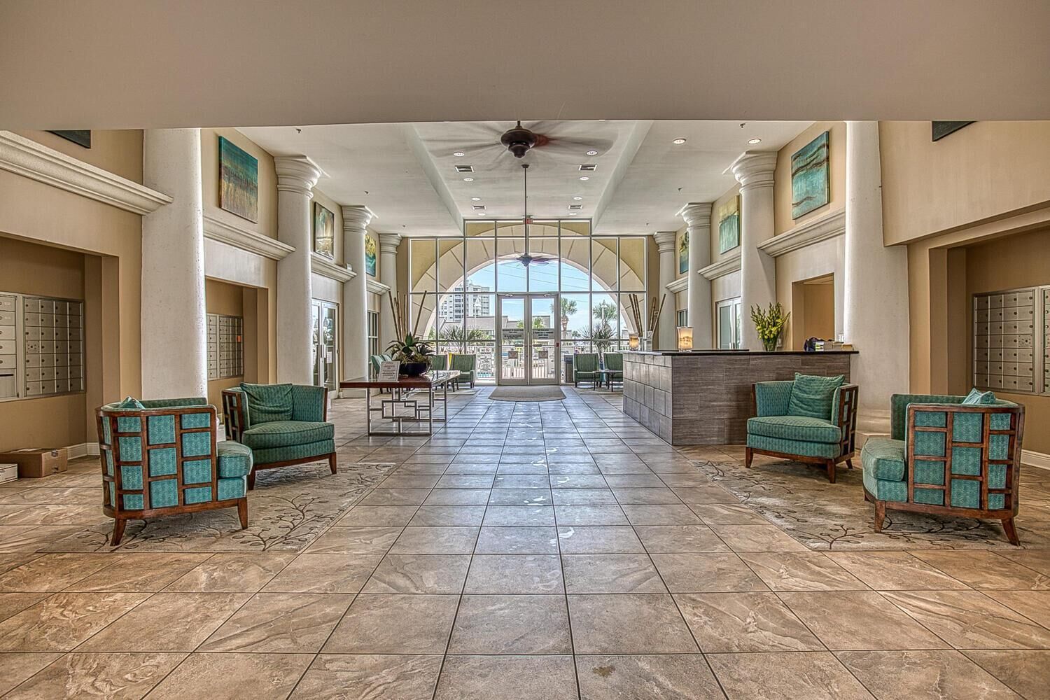 A spacious lobby with a high ceiling, large windows, and a central seating area with chairs.
