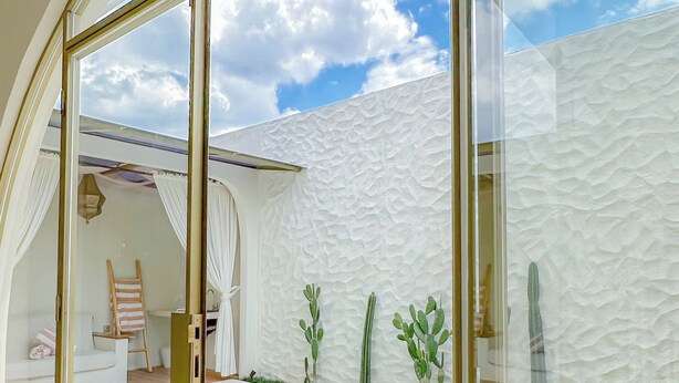 A modern pool area with glass doors, a white textured wall, and a clear sky view.
