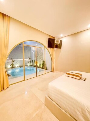 Ein Schlafzimmer mit einem großen Bett, Blick auf einen Swimmingpool durch eine Glastür und einem an der Wand montierten Flachbildfernseher.