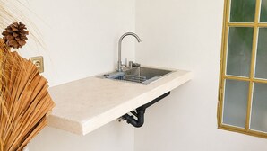 A bathroom with a built-in sink, a white wall, a wooden floor, and a decorative pine cone arrangement.