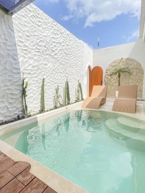 Una piscina amb paret rugosa, zona de fusta i arc de pedra.