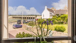 A view of a white house with a stone bridge in the background, a parking area with cars, and some greenery in the foreground. - Charming three-level house - 2 guests (Portbail)