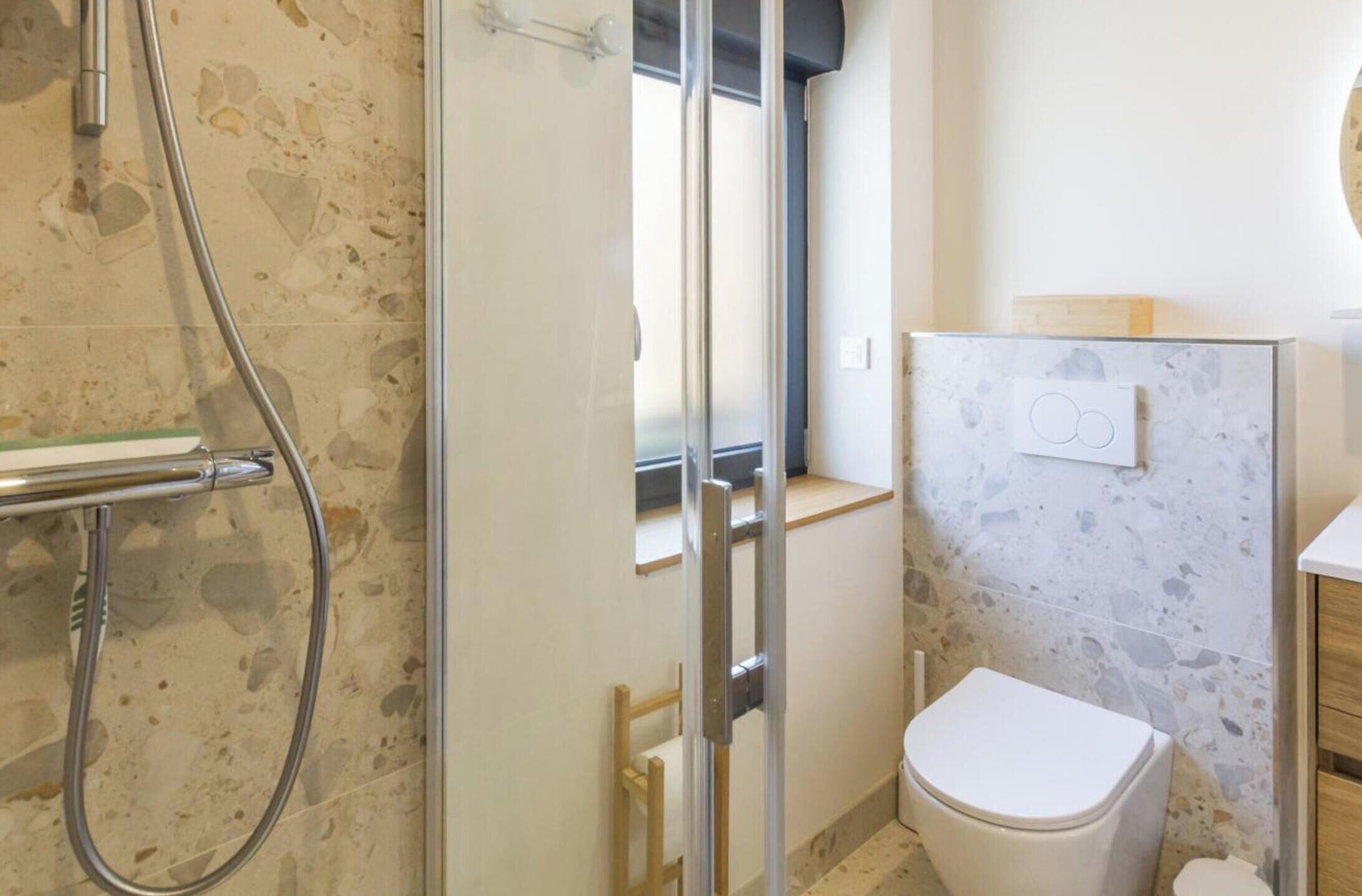 A bathroom with a shower, toilet, and marble walls.