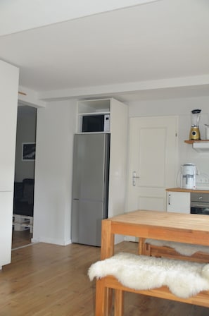 A compact kitchen with a refrigerator, a coffee maker, and a wooden table.
