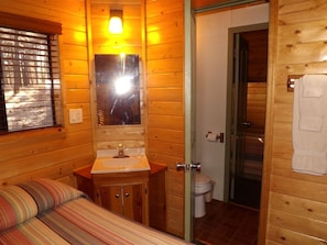 L’intérieur d’un chalet en bois, avec un lit, un lavabo et des toilettes.