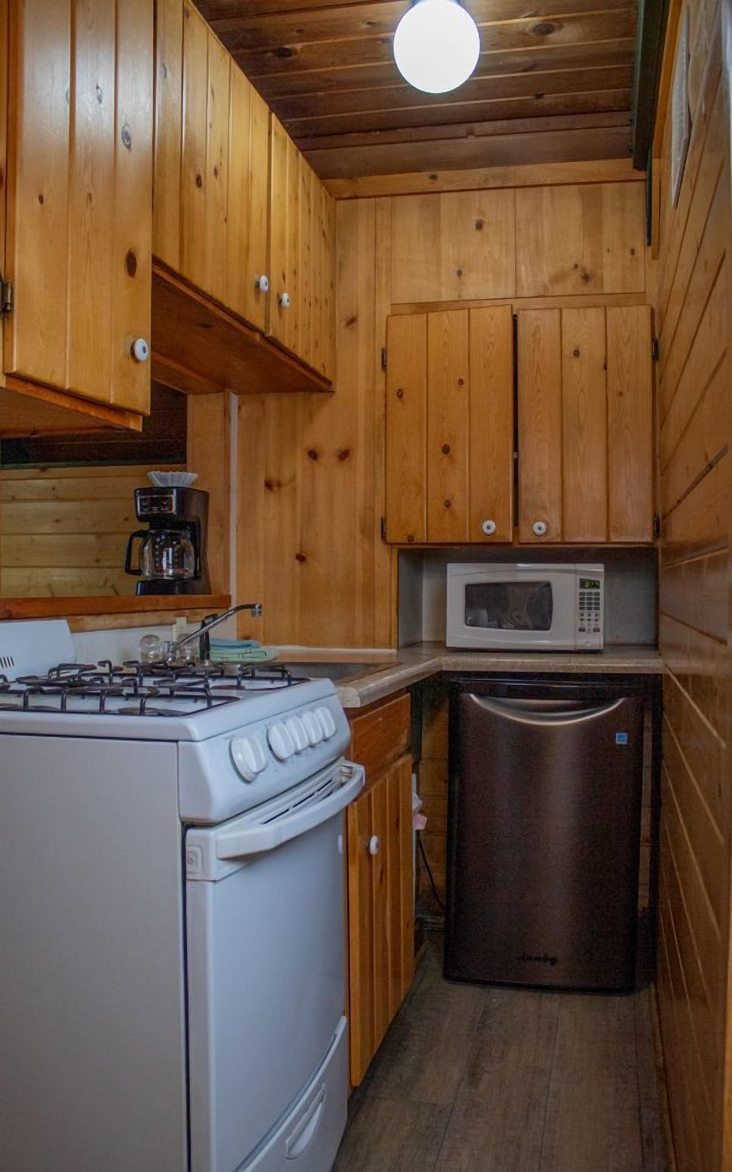 A compact kitchen with wooden cabinets, a gas stove, a microwave, and a dishwasher.