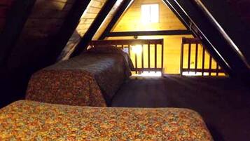Une chambre mansardée avec un plafond en pente, deux lits avec une literie à motifs floraux et une vue sur une structure en bois à l’extérieur.