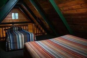 A room with a sloped ceiling, a bed with a striped bedspread, and a chair with a striped cushion. - Quaint Cabin with Lofted Interior and Deck in Arizona (Flagstaff)