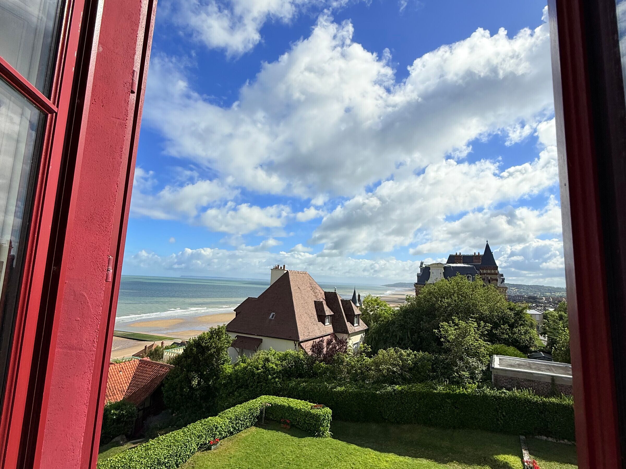 A view of a coastal area with a beach, a large castle-like building, and a house with a red door.