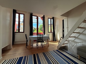 Ein Zimmer mit Tisch und Stühlen, einem Fenster mit Blick, einem Heizkörper und einer Treppe.