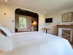 A bedroom with a large bed, a fireplace, a television, and a window with a view of greenery.