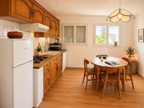 A kitchen with wooden cabinets, a white refrigerator, a stove, and a dining table with chairs. - Spacious apartment in countryside - 4 guests (Villers-sur-Mer)
