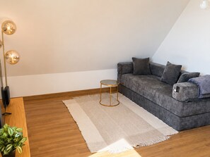 A modern living room with a grey sofa, a small round table, a floor lamp, and a potted plant. - Spacious apartment in countryside - 4 guests (Villers-sur-Mer)