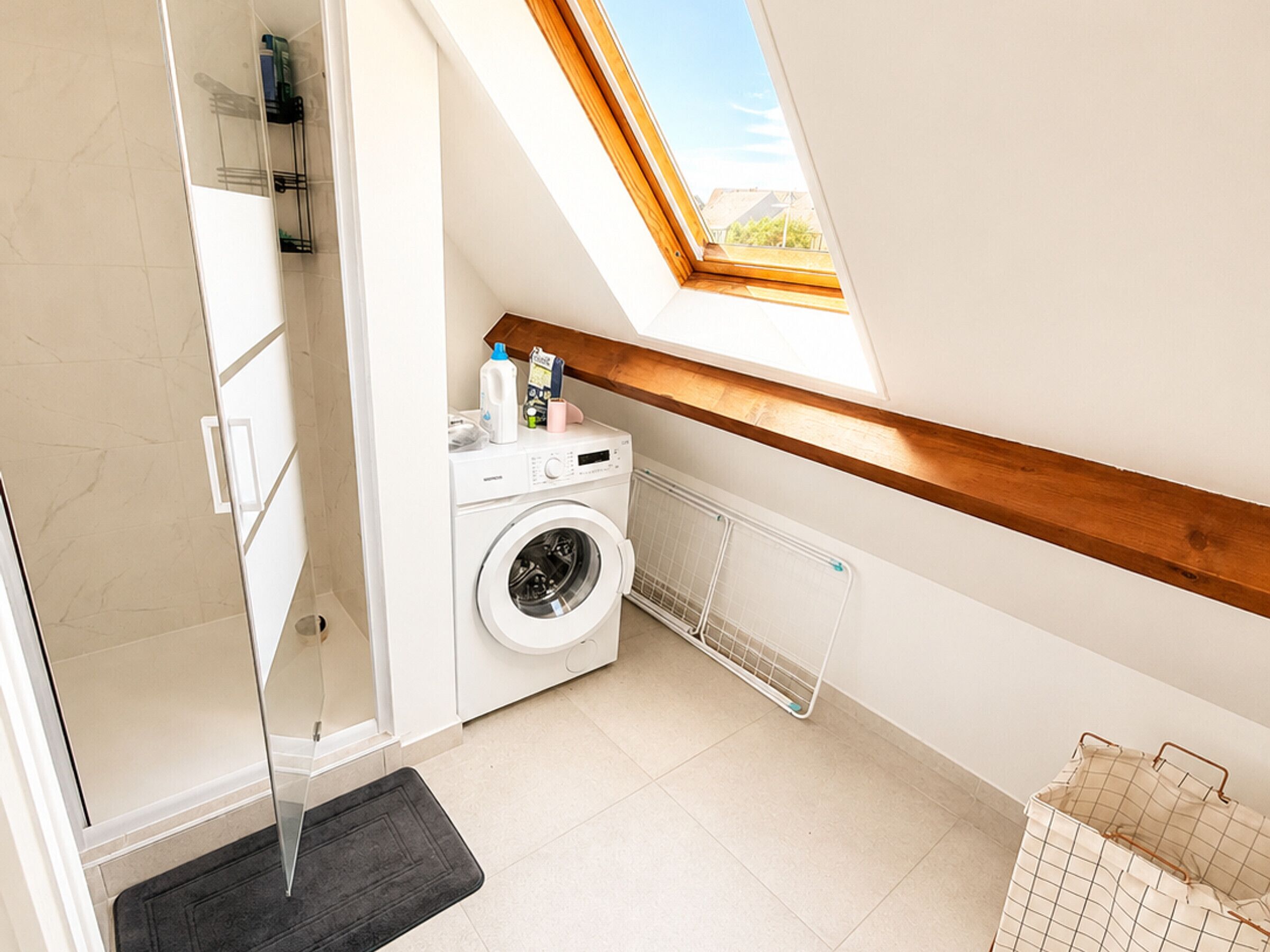 A compact laundry room with a washing machine, a drying rack, and a skylight.