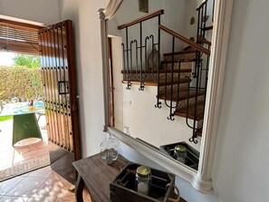Ein Zimmer mit Holztisch, Spiegel, der eine Treppe reflektiert, und einer Tür zu einem Außenbereich.