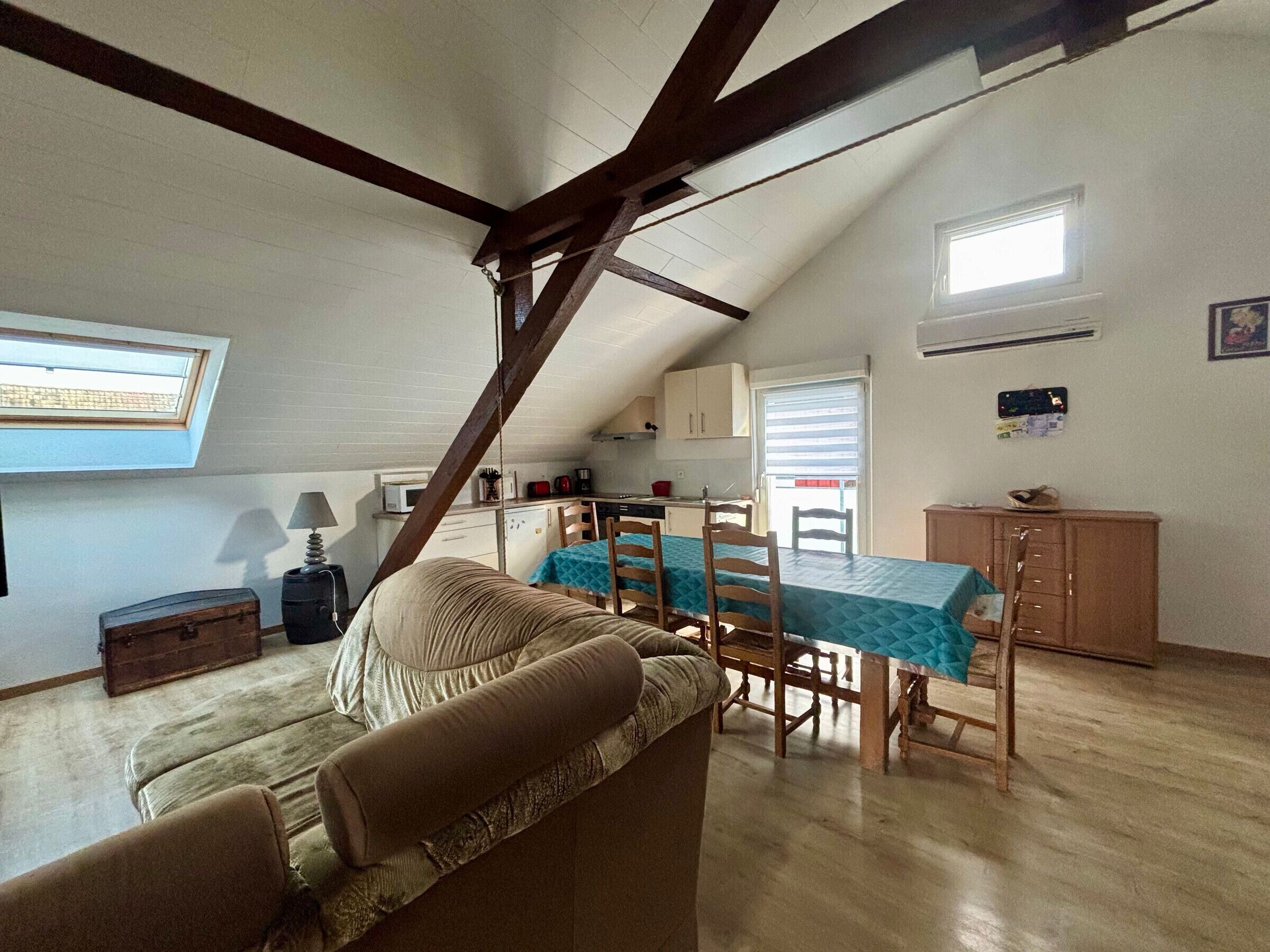 Une pièce de style loft avec un plafond en pente, une table à manger avec des chaises, un canapé, un coin cuisine et une fenêtre.