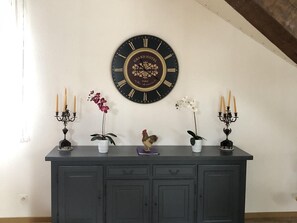 A dark wooden console table with a large wall-mounted clock, two potted plants, and two candelabra with candles.
