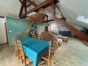 A loft-style room with a dining table, chairs, a sofa, and a staircase.