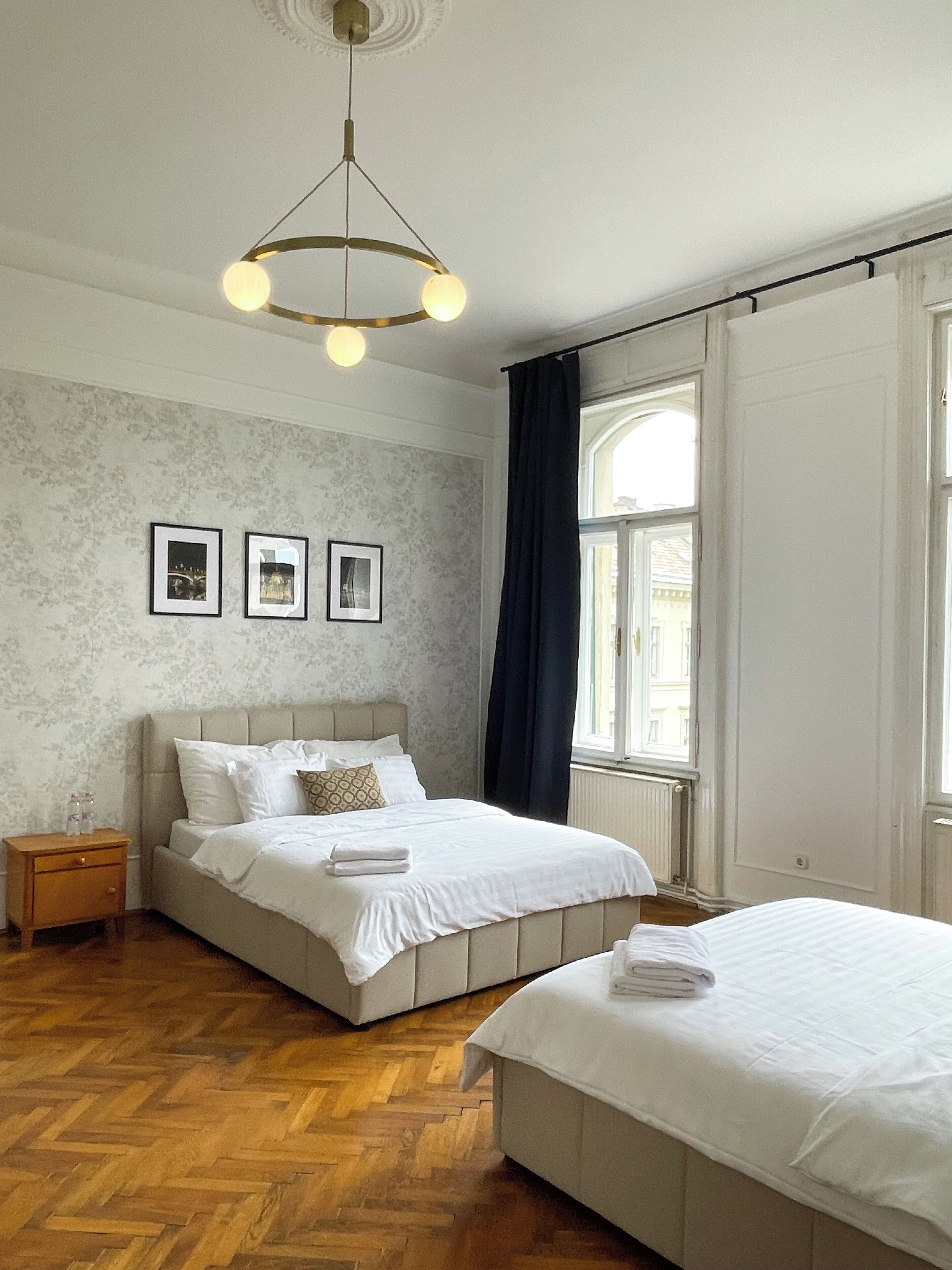 A bedroom with a bed, a nightstand, a window with curtains, and a hanging light fixture.
