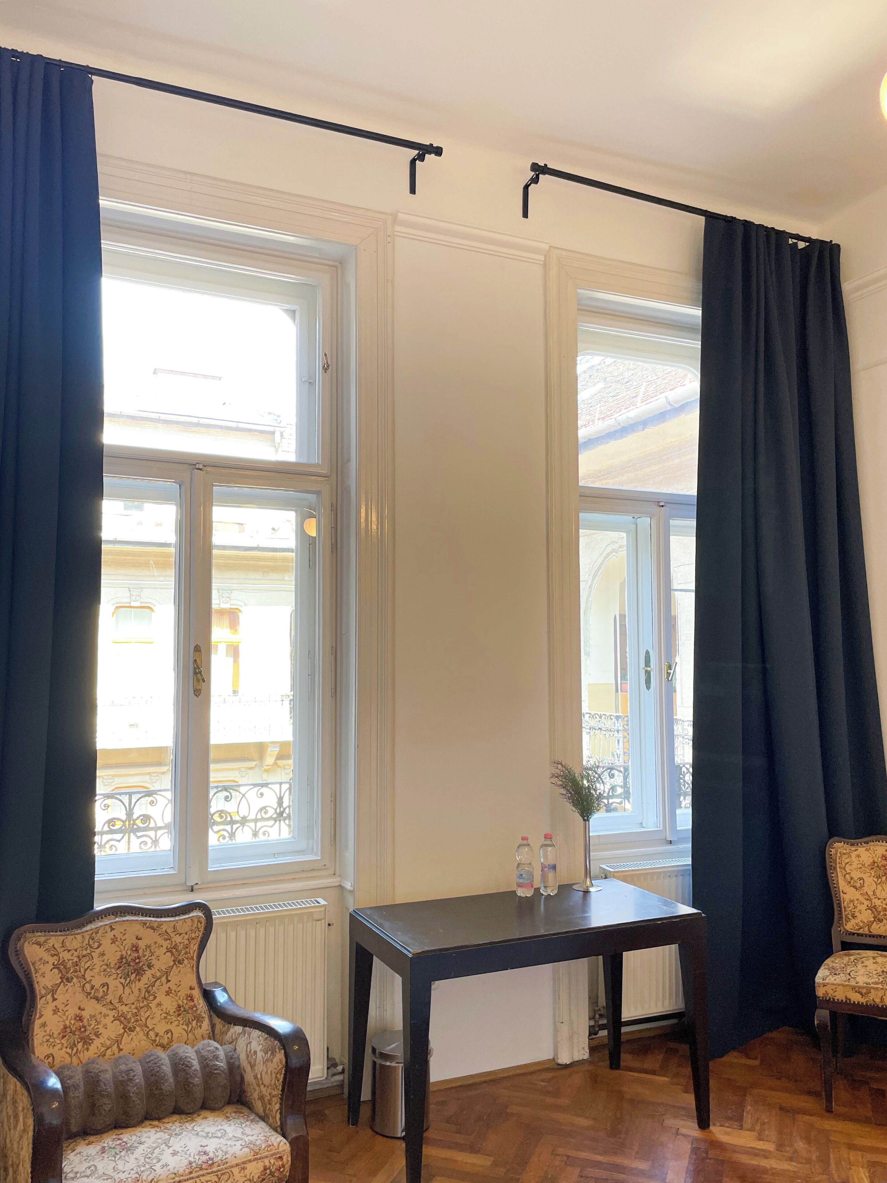 A room with a wooden floor, a table with two bottles, a chair, and a window with curtains.
