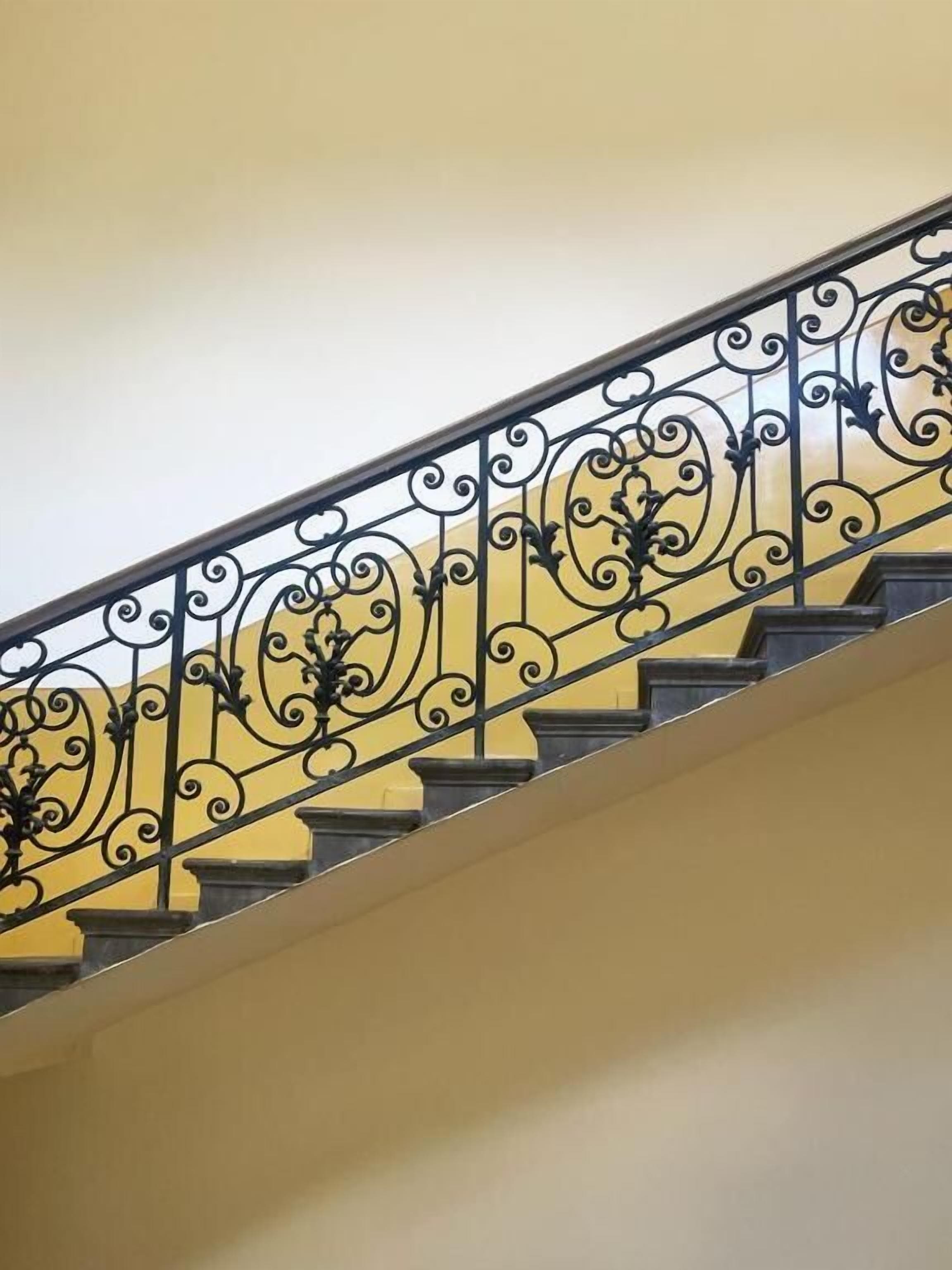 A staircase with ornate black metal railings and a yellow wall.