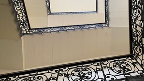 A balcony with ornate black metal railings and a beige wall.