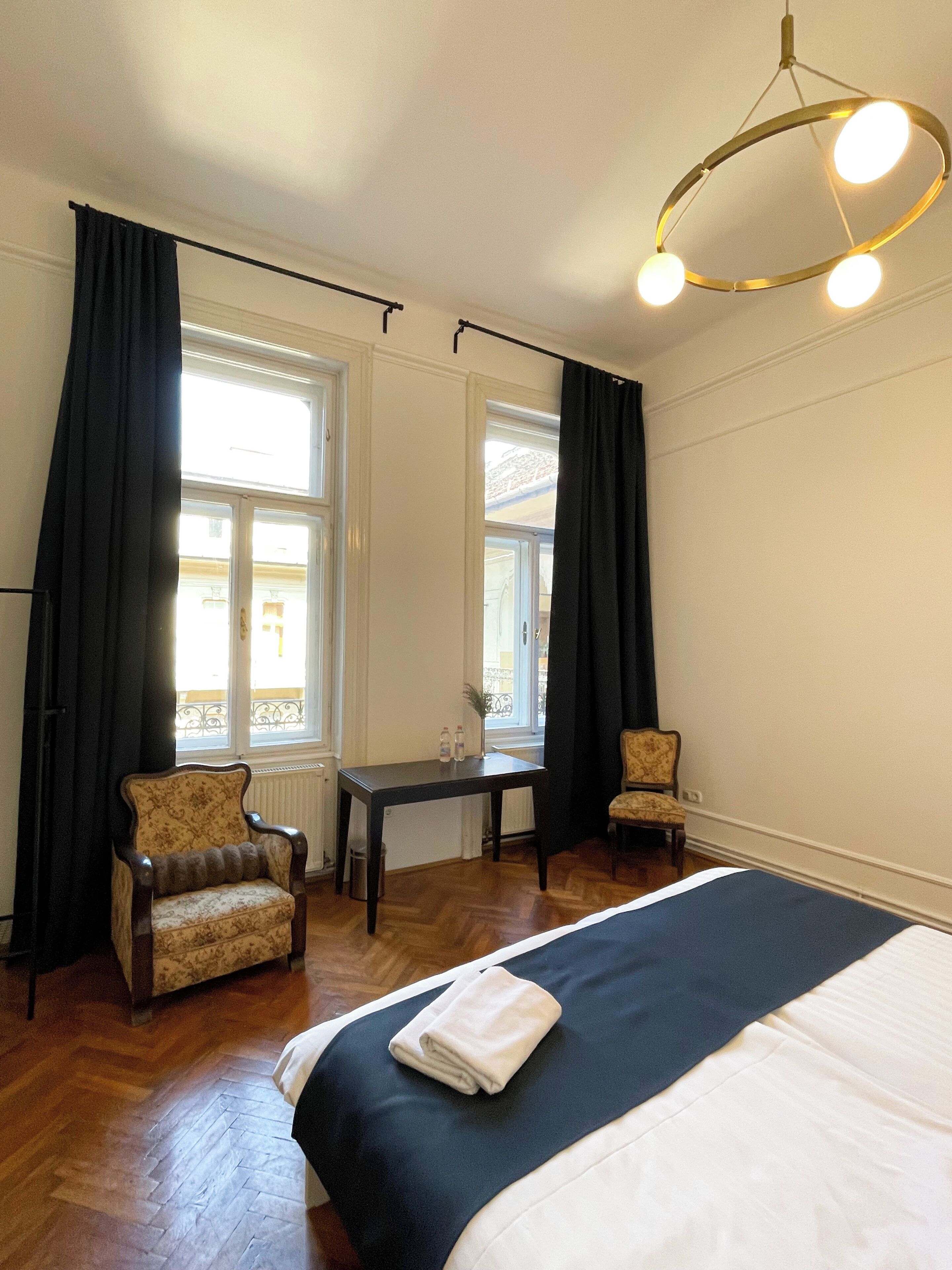 Ett hotellrum med en säng, två fåtöljer, ett bord och en kristallkrona.