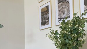 A room with a black leather chair, a round marble table with a vase and glasses, and framed pictures on the wall.