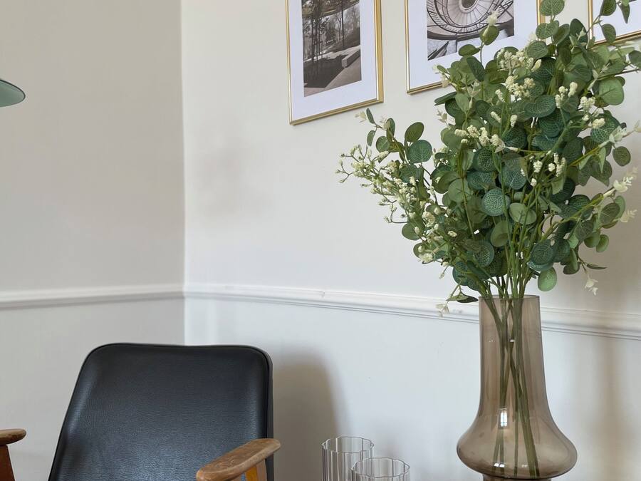 A room with a black leather chair, a round marble table with a vase and glasses, and framed pictures on the wall.
