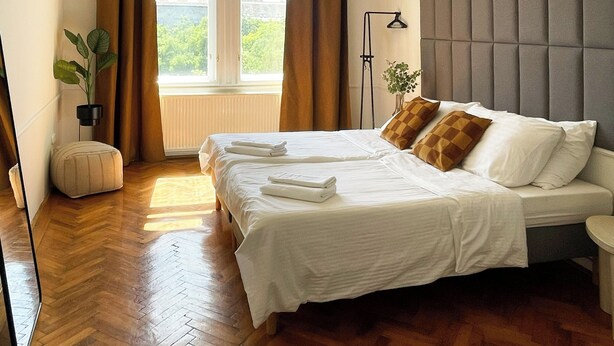 A bedroom with a bed, a window with curtains, a plant, and a chandelier.