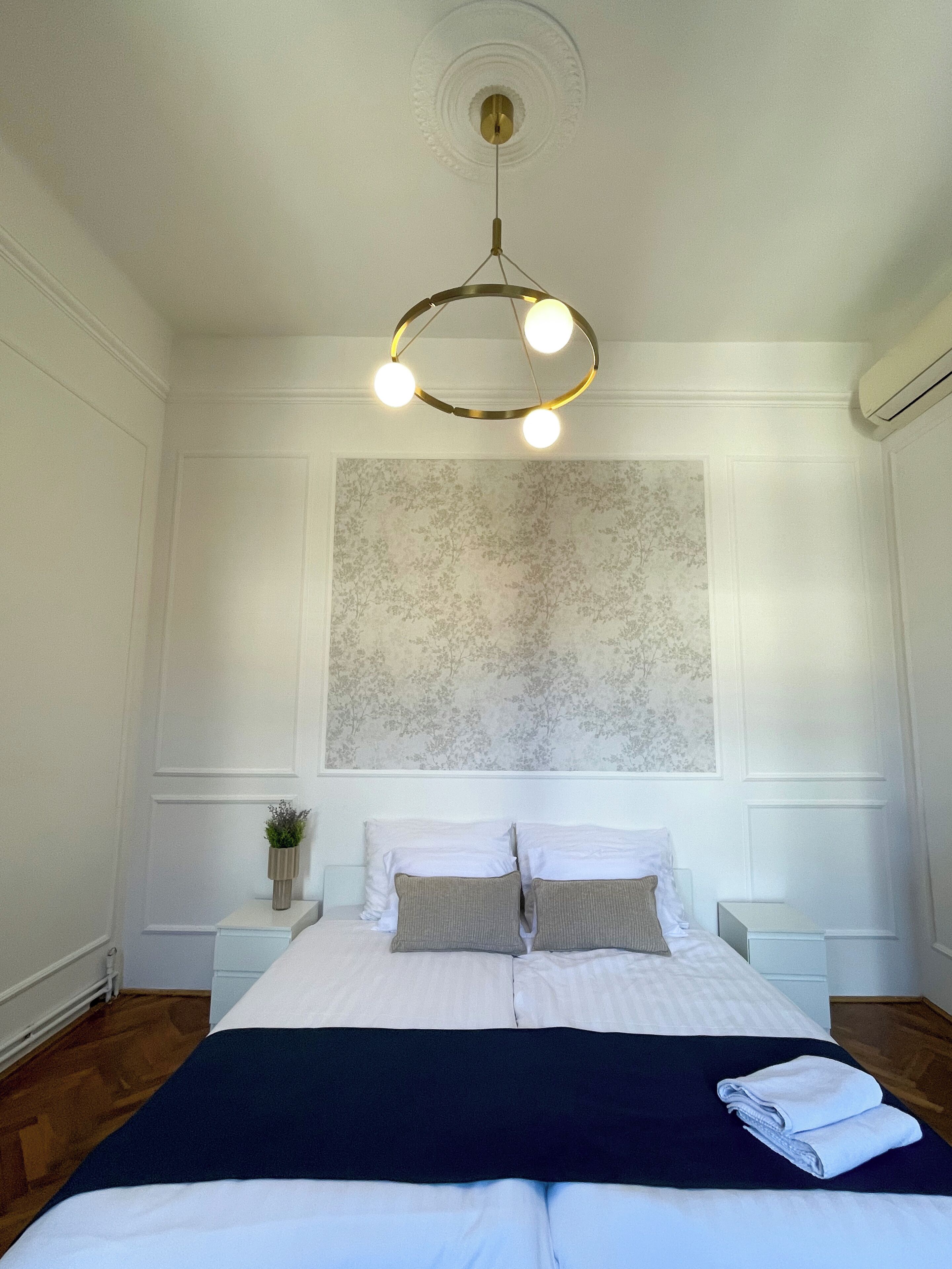 Une chambre à coucher comprenant un lit, des tables de chevet, un luminaire fixé au mur et un papier peint à motifs floraux.