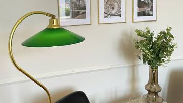 Una habitación con una silla negra, una lámpara de pie verde, una pequeña mesa redonda con un florero y seis cuadros en la pared.