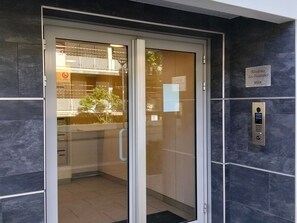 Ein moderner Hotelzugang mit Glastür, einem digitalen Aufzugbedienteil und einem Schild mit der Aufschrift 'Residence Les Oceaines ASIA'.