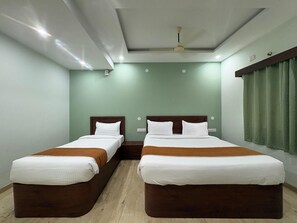 A hotel room with two beds, a ceiling fan, and a window with curtains. - Hotel Raasaa Grand Rooms (Bengaluru)