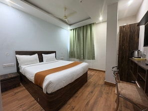Ein Hotelzimmer mit Bett, Schreibtisch, Stuhl, einem Fenster mit Vorhängen und einem Deckenventilator.