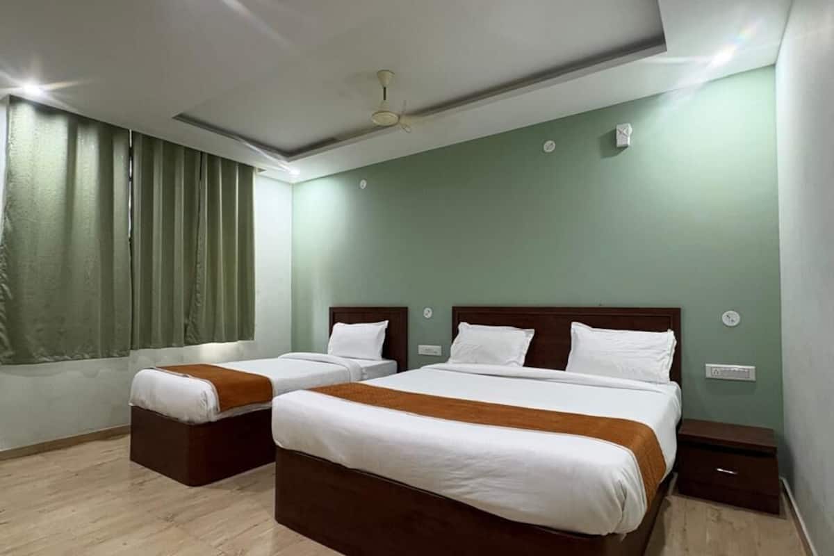 Hotellihuone, jossa on kaksi sänkyä, puulattia, vihreä seinä ja ikkuna, jossa on verhot.